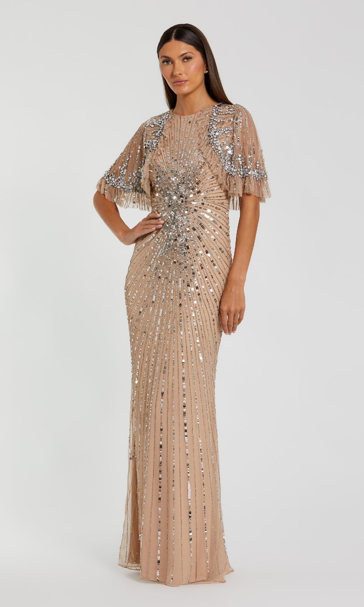 A woman models the Mac Duggal 23044 Capelet Long Beaded Formal Dress, a floor-length nude gown with silver sequins, fitted silhouette, and short sleeves, standing against a plain light background.
